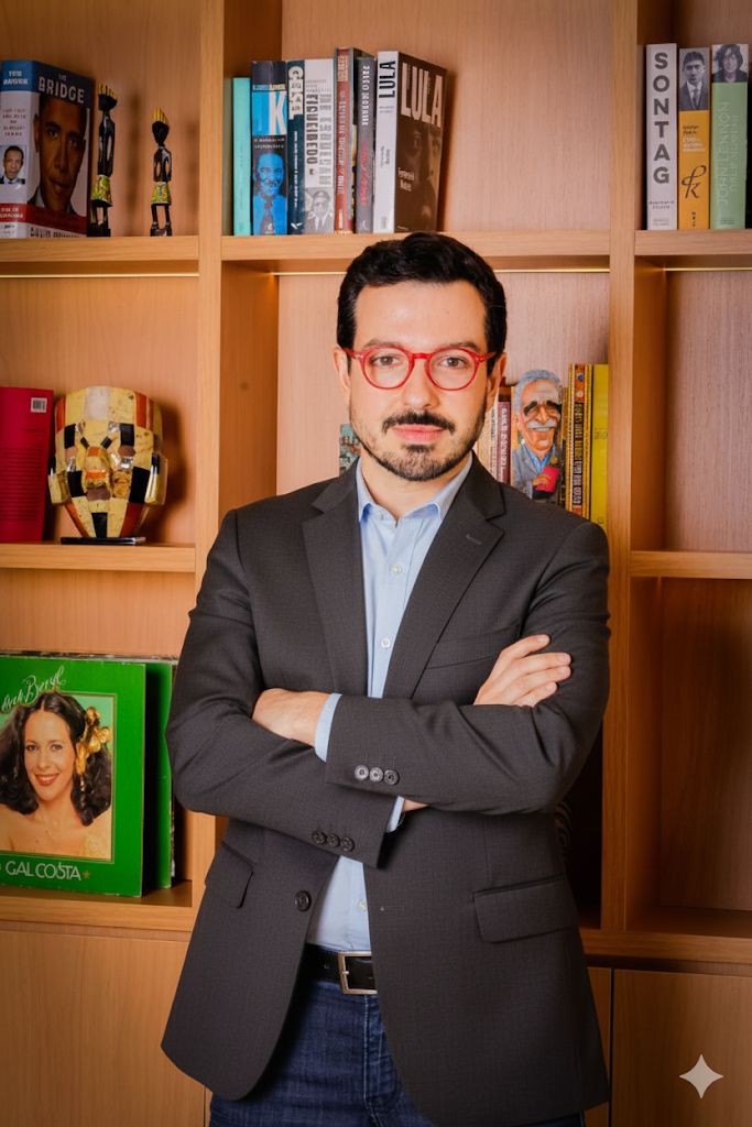 Guilherme Amado diante de uma estante de livros